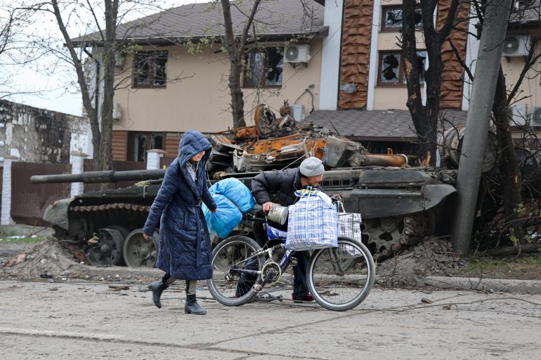 Local civilians walk past a tank destroyed during heavy fighting in an area controlled by Russian-backed separatist forces in Mariupol.