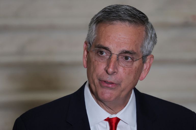 A man in glasses, in a black suit and red tie, speaks a day after midterm elections, in Atlanta, Georgia, U.S. November 9, 2022