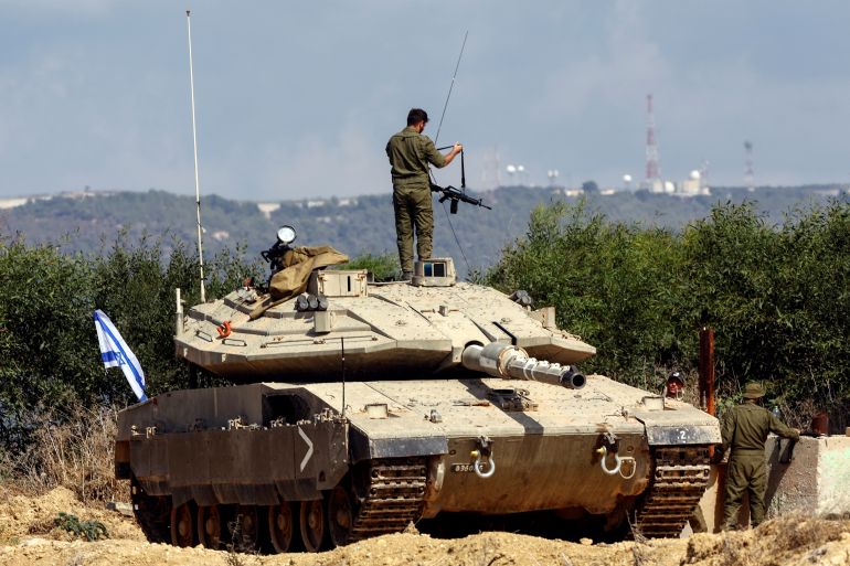 An Israeli soldier holds a rifle by its strap as he adjusts it, while standing atop a tank in Israel's northern border region.