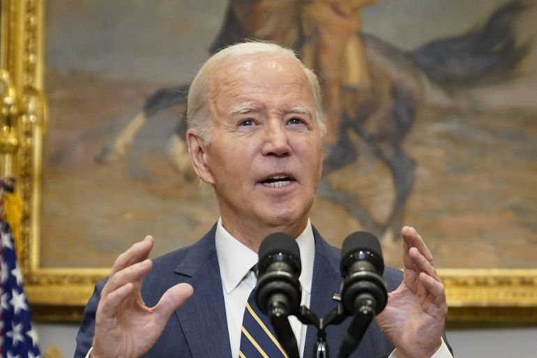 US President Joe Biden speaking from the Roosevelt Room. He is behind a lectern with flags behind him. He is making a point with his hands.