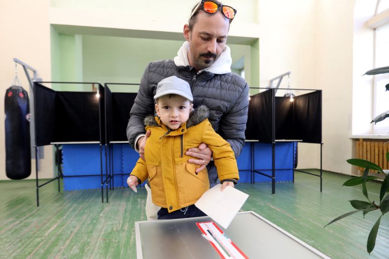 A voter with child prepares to cast a ballot into an urn during the first round of Lithuania's presidential election at a polling station in Vilnius