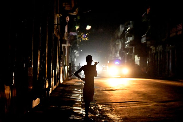A darkened silhouette holds a cellphone up to her ear during a blackout. A car light can be seen on the darkened street.