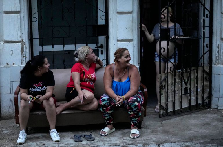 Three women outside a home in Havana, while another opens a metal gate leading inside.