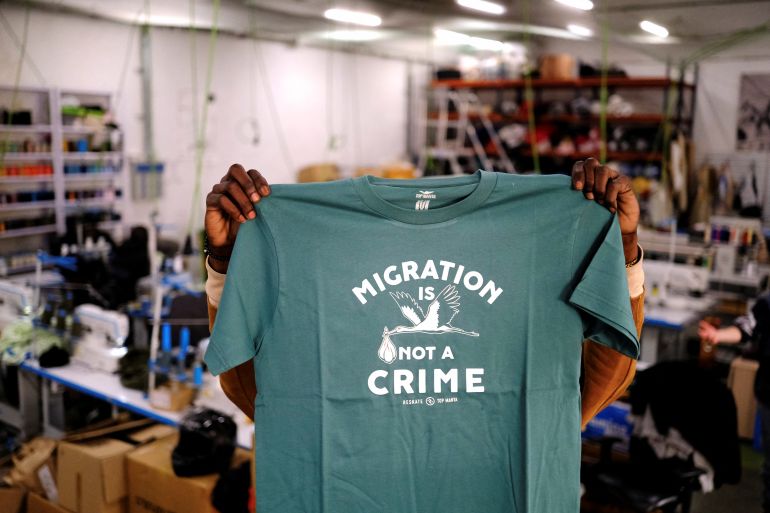 A person holds up a T-shirt with "Migration is not a crime" printed on it.