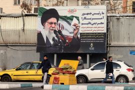 Iranians walk past a billboard showing Iranian supreme leader Ayatollah Ali Khamenei with anti-US rhetoric in Tehran on January 27, 2026.